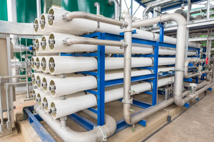 Fotografía de instalaciones de equipos de tratamiento de agua que son tubos blancos y grises en estructura color azul.