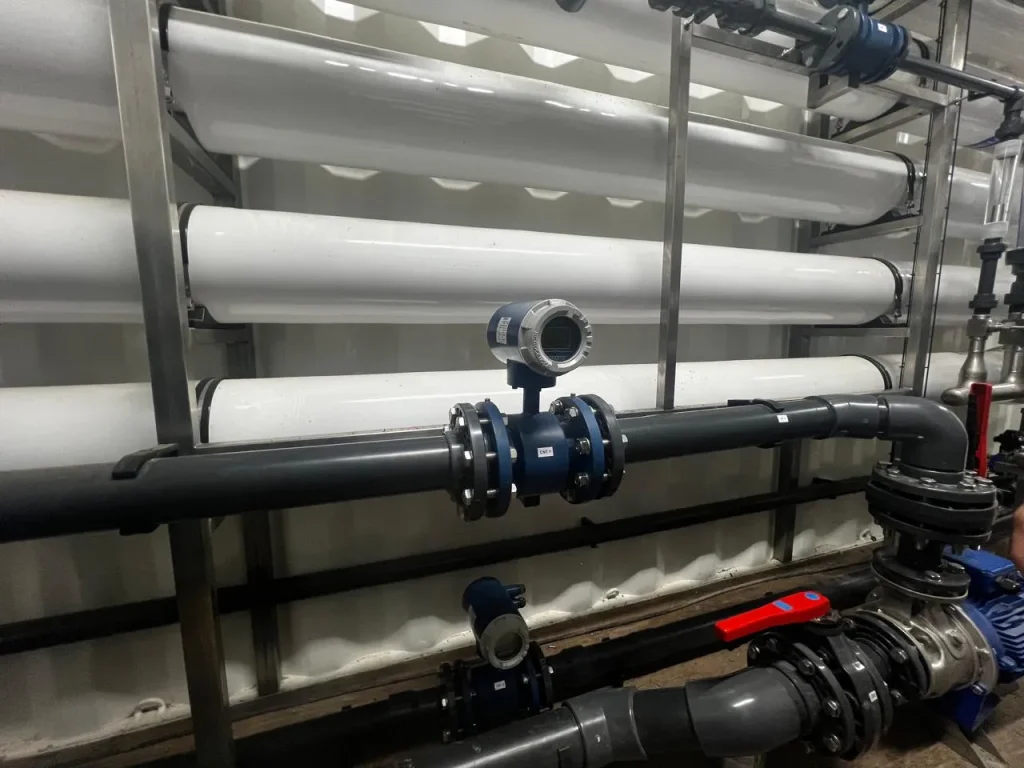 Fotografía de tubos color blanco y negro con maquinaria color azul que son parte de un sistema de osmosis inversa.