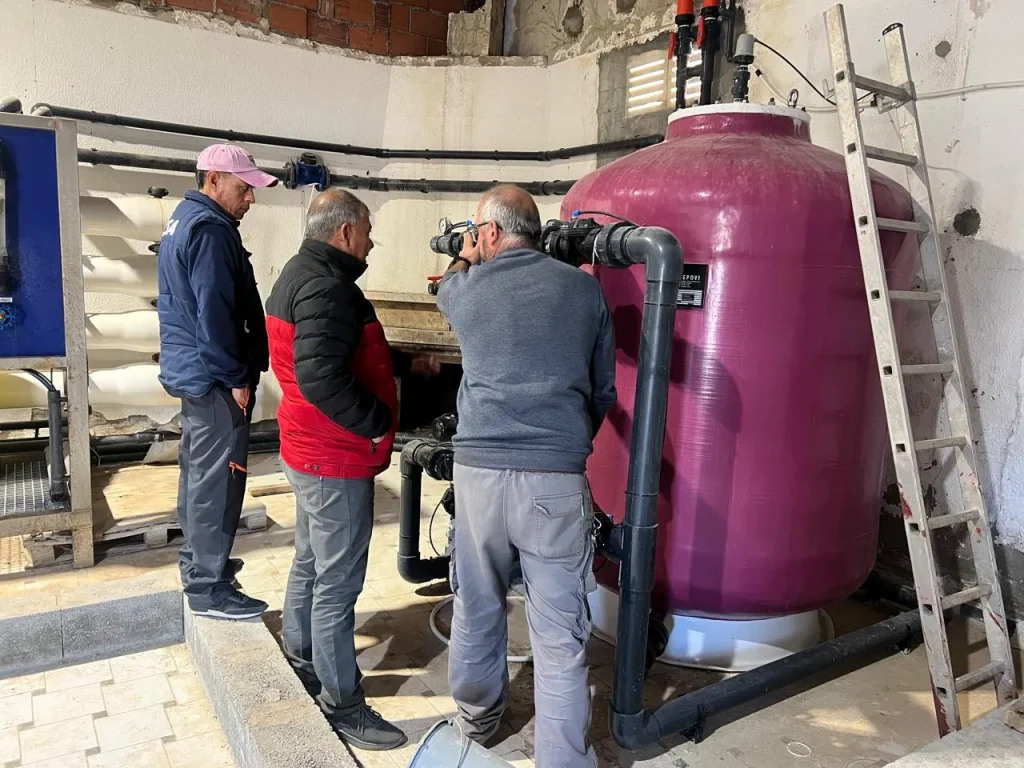 Fotografía de tres personas a lado de un tanque color rojo que es parte de un sistema de osmosis inversa.