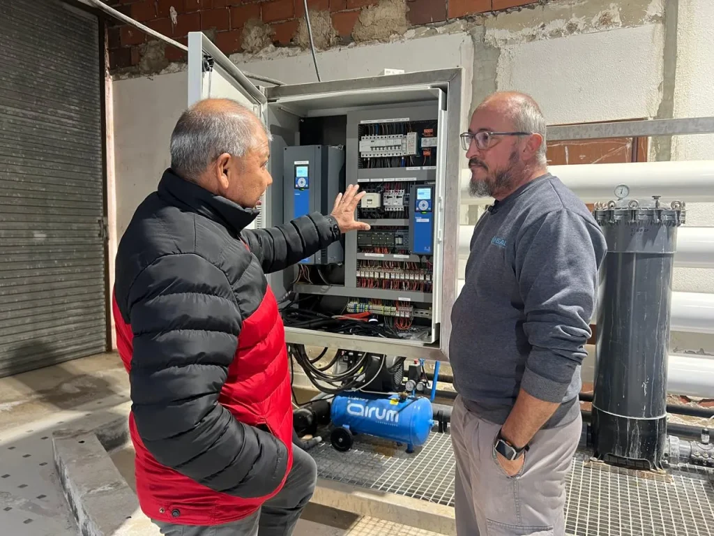 Ósmosis inversa industrial: fotografía de dos hombres de pie conversando frente a una caja con cables.